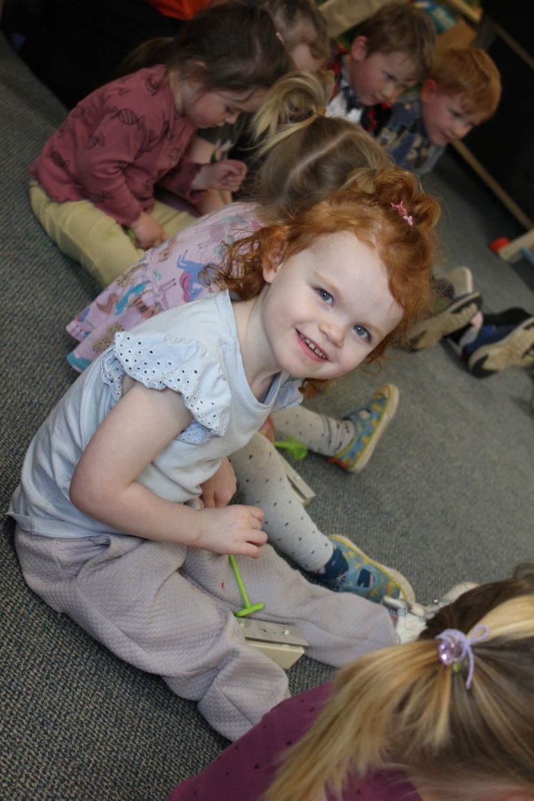 A smiling child sitting on the carpet during a music session