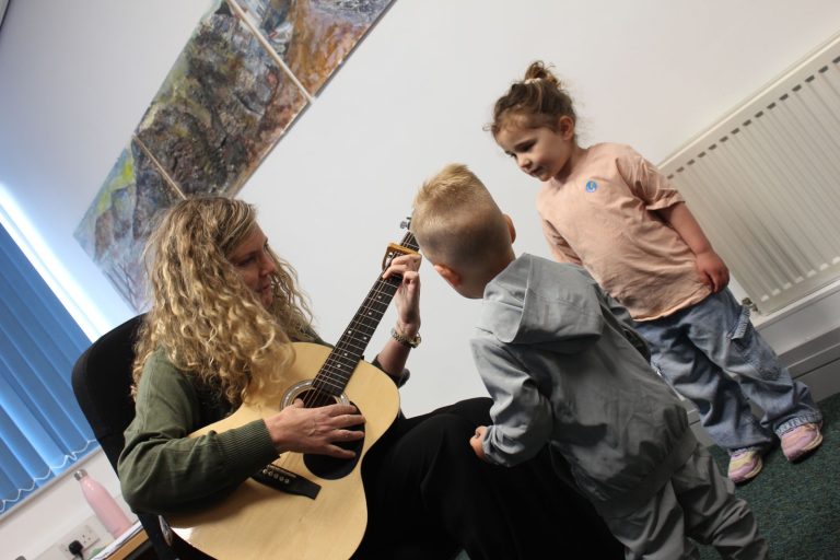 Children gathering round to watch a guitar lesson