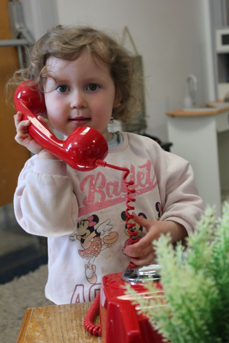 A toddler pretending to talk on a red toy telephone