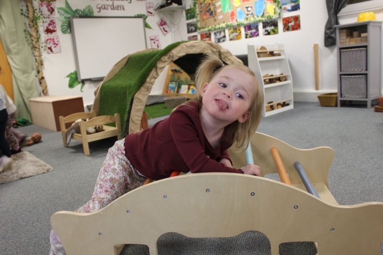 A child playing on a wooden rocker in the toddler room