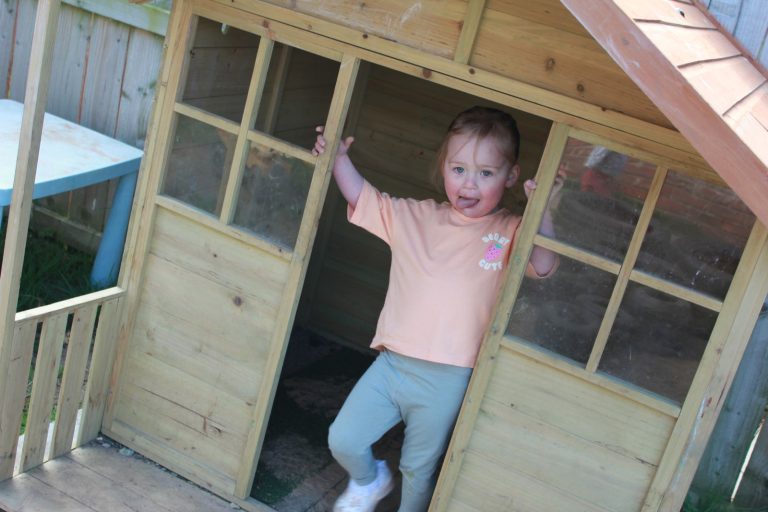 A child waving from the wooden playhouse