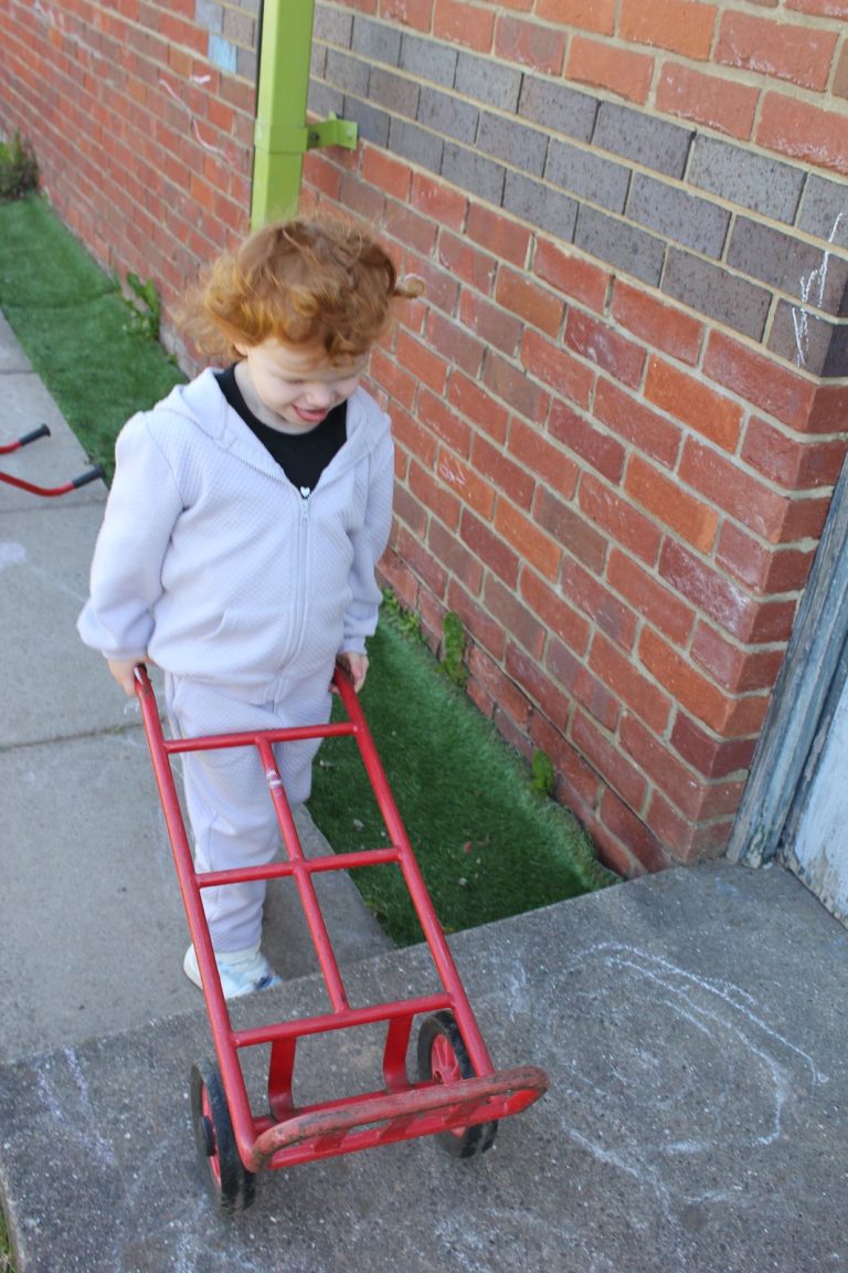 A child pushing a red trolley along the path