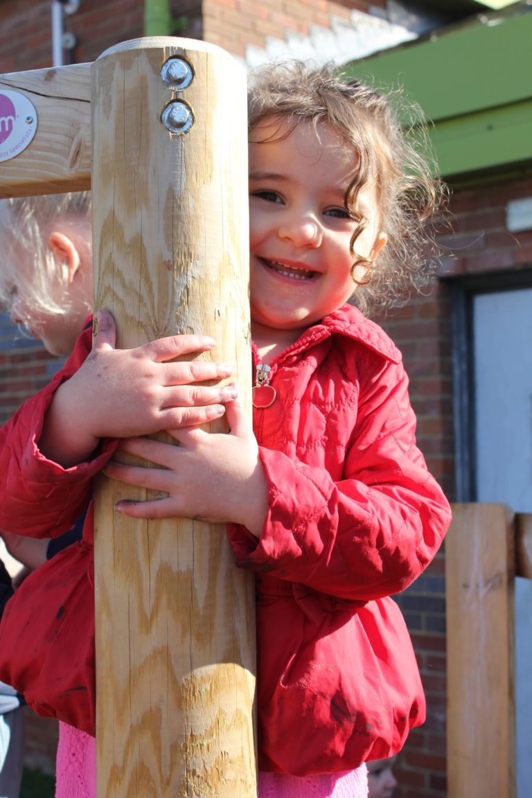 A child hugging a wooden post and smiling