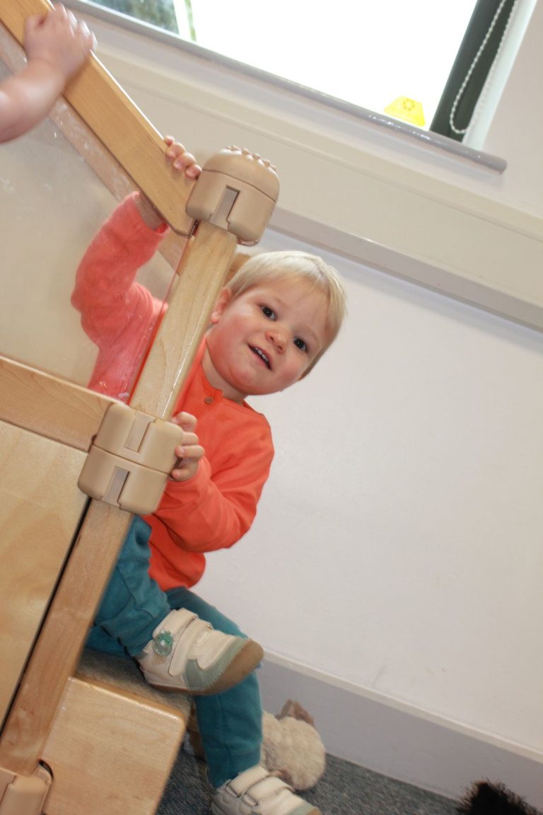 A baby climbing on a wooden frame