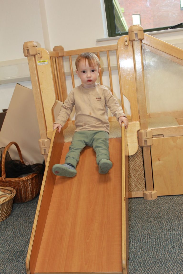 A baby sliding down a small wooden slide